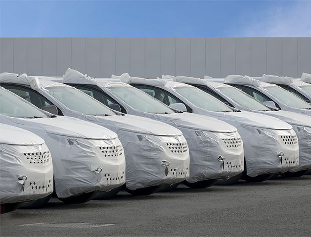 En rekke med nye biler, delvis dekket, klare for eksport eller salg.